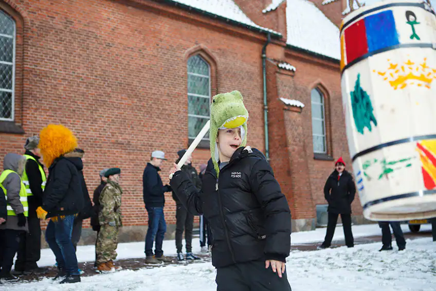 A young boy hits a wooden barrel with a stick to try and get the candy out