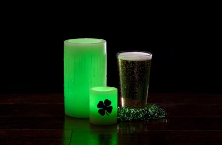 Glowing green wax candles and glass of beer for St. Patrick's Day Celebration - Stock Image