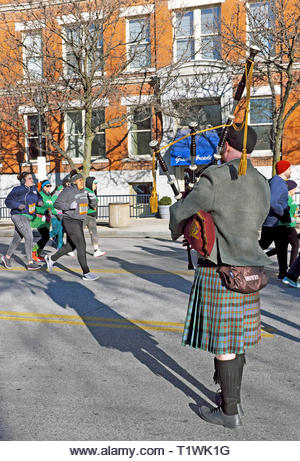 A kilt-clad bagpiper plays as participants in the St. Patricks Day race by in the Warehouse District of Cleveland, Ohio. - Stock Image