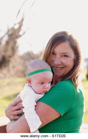 Woman holding newborn baby outside in sunlight on St Patty's Day - Stock Image