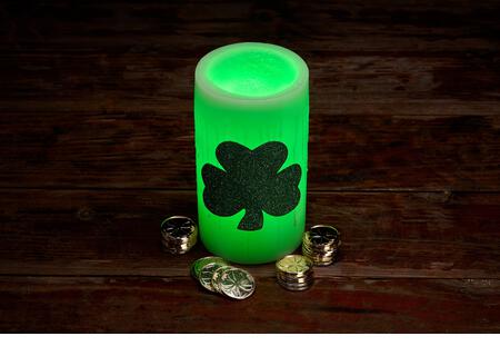 Glowing green wax candle and stacks of gold coins for St. Patrick's Day Celebration - Stock Image