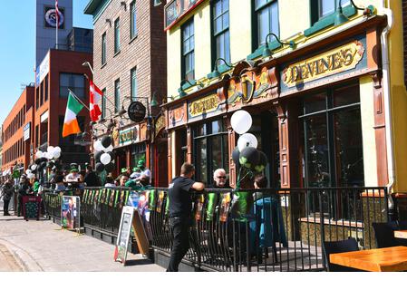 Ottawa, Canada - March 17, 2021: A much smaller crowd than usual, because of Covid-19 restrictions, celebrates St. Patrick's Day at the popular Irish Pub the Irish Village.  Warm weather made patio seating possible. - Stock Image