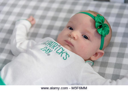little baby girl laying in bed with shamrock headband and blue eyes on st paddys day - Stock Image