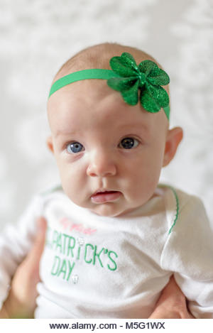 Irish baby with big blue eyes wearing St Patricks Day outfit and shamrock headband - Stock Image