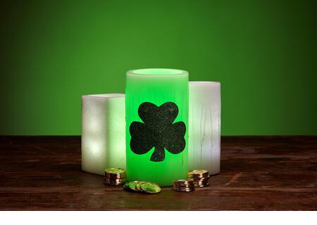 Glowing green wax candles and stacks of gold coins for St. Patrick's Day Celebration - Stock Image